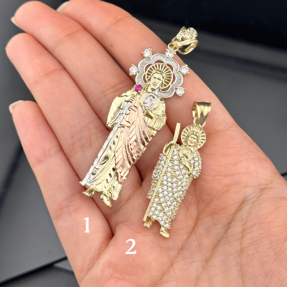 Two gold pendants on a hand, one larger and more detailed than the other.
