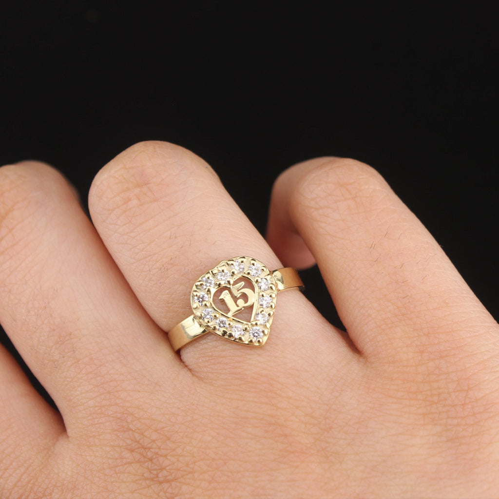 Gold ring with a heart design on a hand against a black background