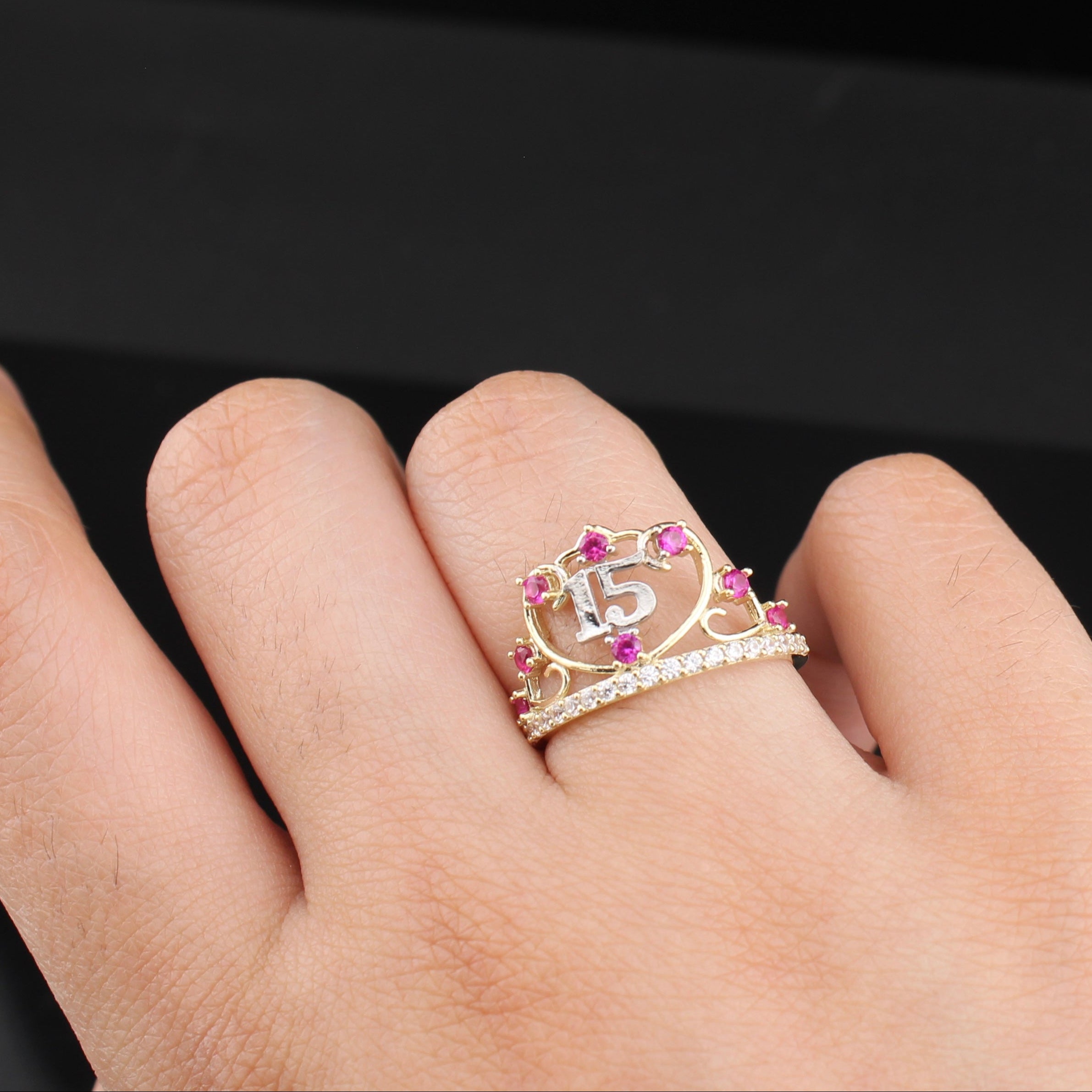 Hand wearing a ring with a number 15 and gemstones on a dark background